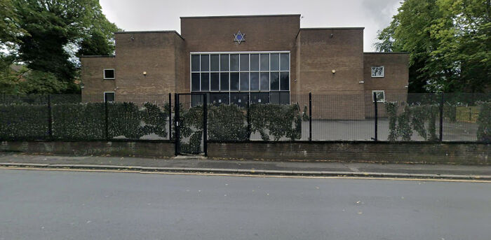 Manchester synagogue exterior with fence and Star of David symbol on brown brick building on a cloudy day.