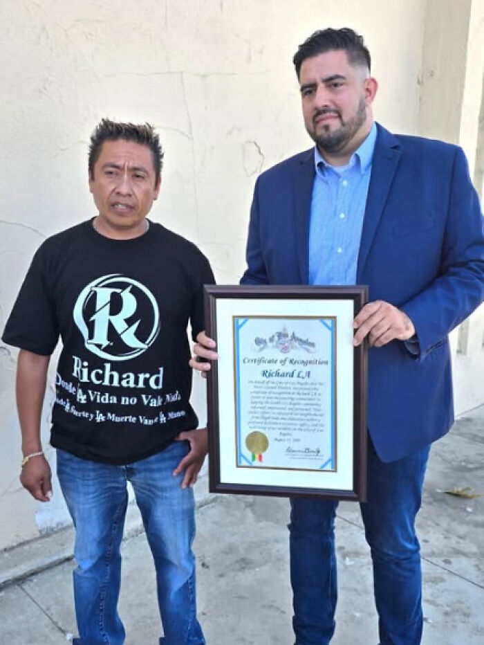 Two men standing outside, one holding a framed certificate, related to LA TikToker filming ICE raids and immigration events.