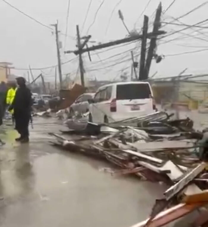 Debris and damaged vehicles line a flooded street as Hurricane Melissa causes devastation across Jamaica.