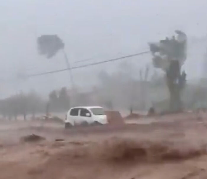 Flooded street with a white car partially submerged during Hurricane Melissa devastation in Jamaica with strong winds and heavy rain.