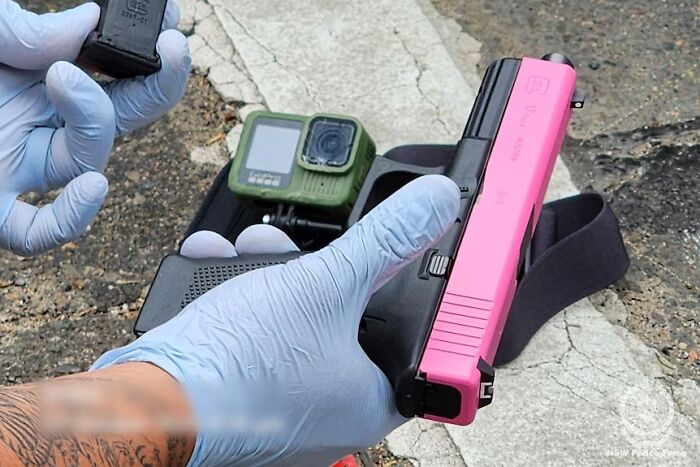 Gloved hands holding a pink handgun and magazine, with a body camera on the ground, linked to alleged assassins footage.