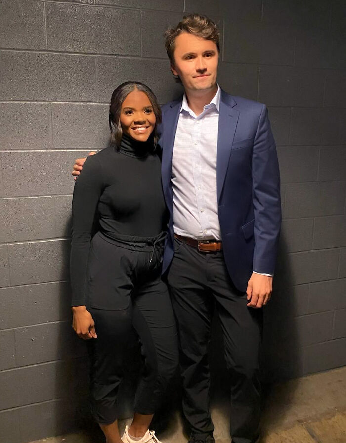 Candace Owens and Charlie Kirk posing together against a gray wall, candid moment in casual and formal attire.