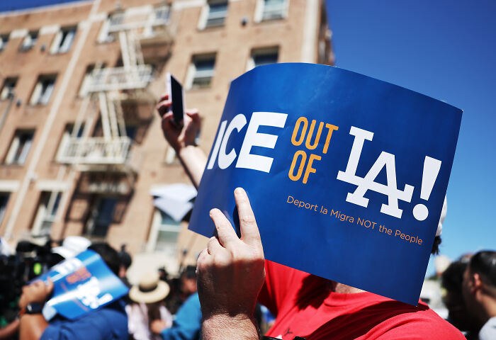 Protesters holding ICE out of LA signs during anti-ICE demonstration in urban area with building in background