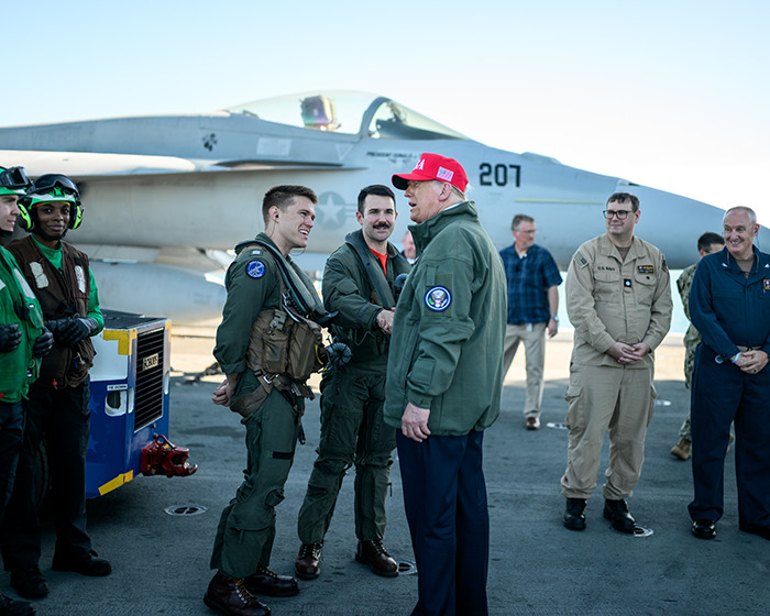 Military personnel and a leader shaking hands on aircraft carrier deck amid Venezuela war tensions and military buildup.