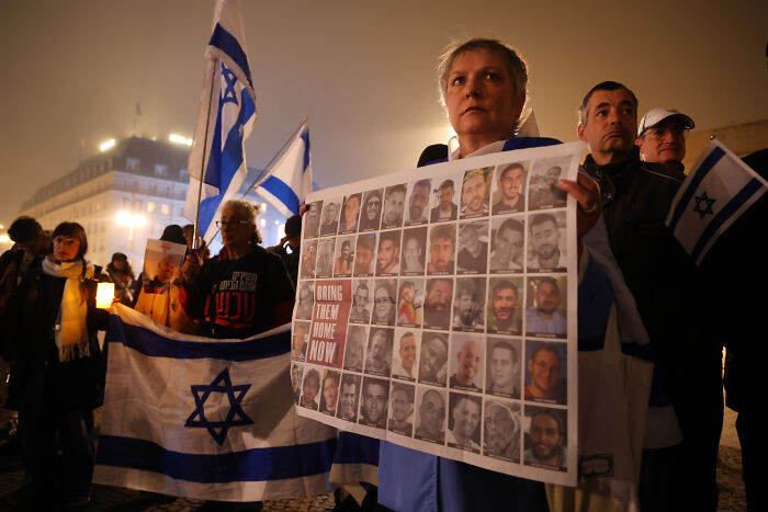 People holding Israeli flags and a poster with hostage photos during a vigil amid Hamas and Israel ceasefire doubts.