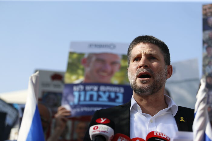 Man speaking at a podium with microphones, addressing Hamas hostage release and Israel ceasefire commitment concerns.