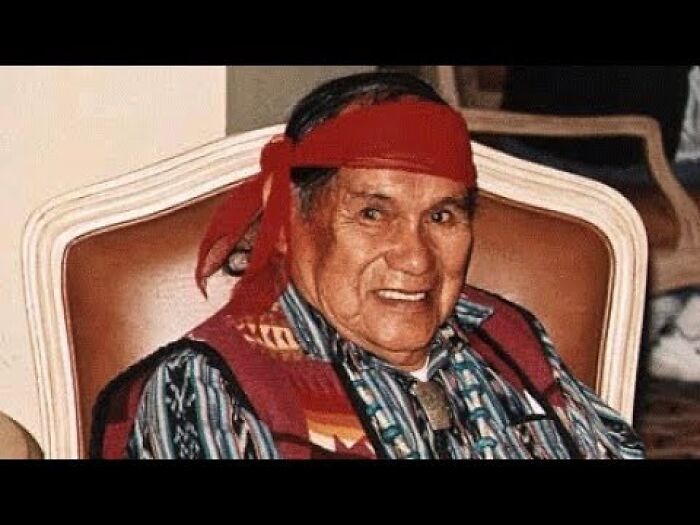 Elderly Native American man wearing a red headband, traditional clothing, linked to ancient Hopi prophecy and red cap figure.