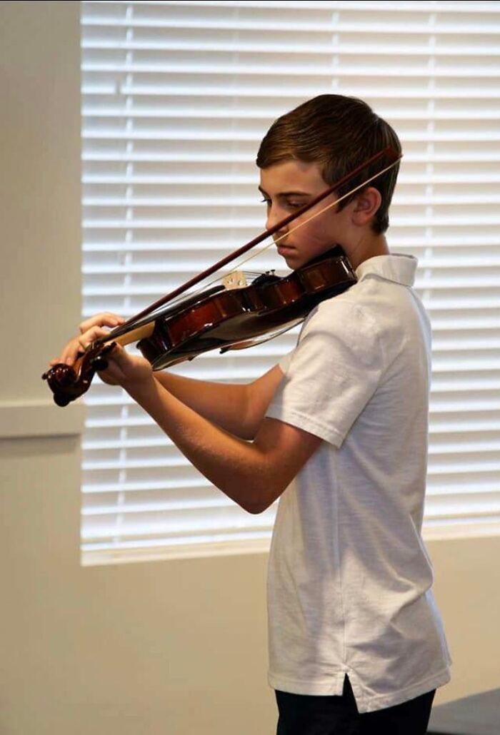 Young boy focused on playing violin indoors with window blinds in the background, related to Florida man case keywords.