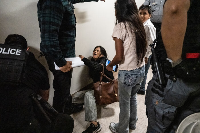 Federal agents arrest woman during Chicago apartment building immigration raid with multiple people in distress inside hallway.
