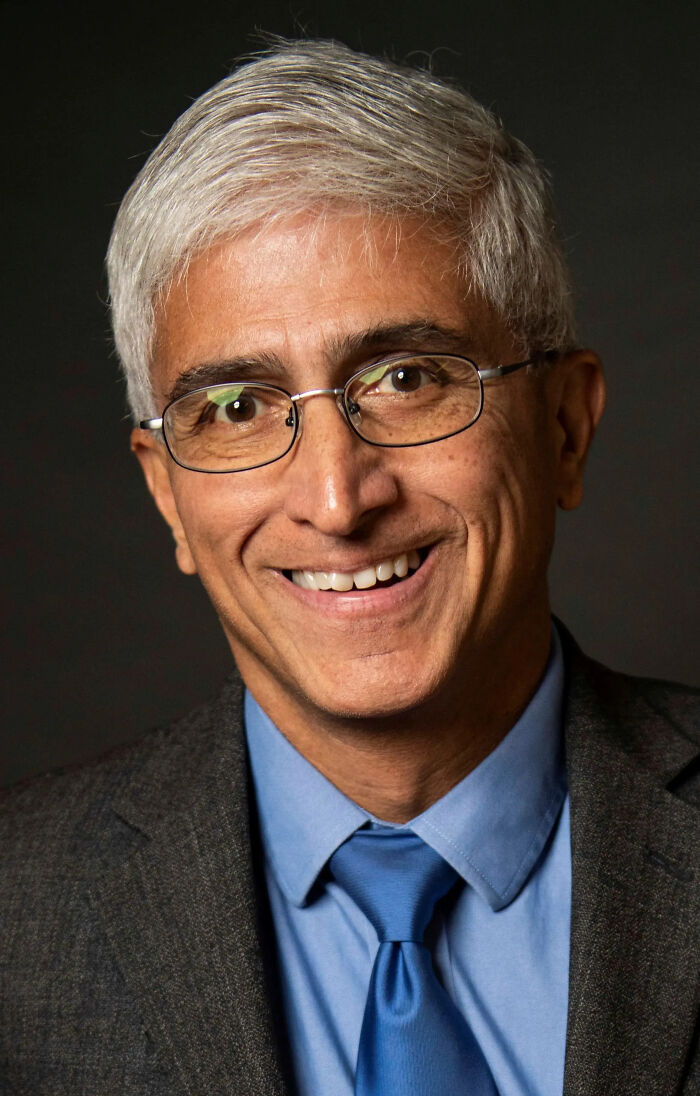 Portrait of a smiling man with glasses, silver hair, and a blue tie representing journalist in Karoline Leavitt text clash.