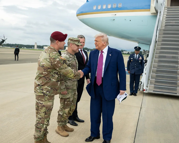 Donald Trump shaking hands with military personnel on an airport tarmac amid Venezuela and Colombia political tension.