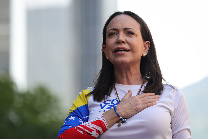 Woman wearing a colorful shirt with a hand on her chest, symbolizing patriotism, related to Trump missing out on Nobel Peace Prize.