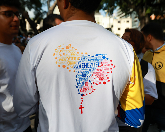 Person wearing a shirt with a colorful map of Venezuela made of words during a public gathering related to Venezuela analysis.