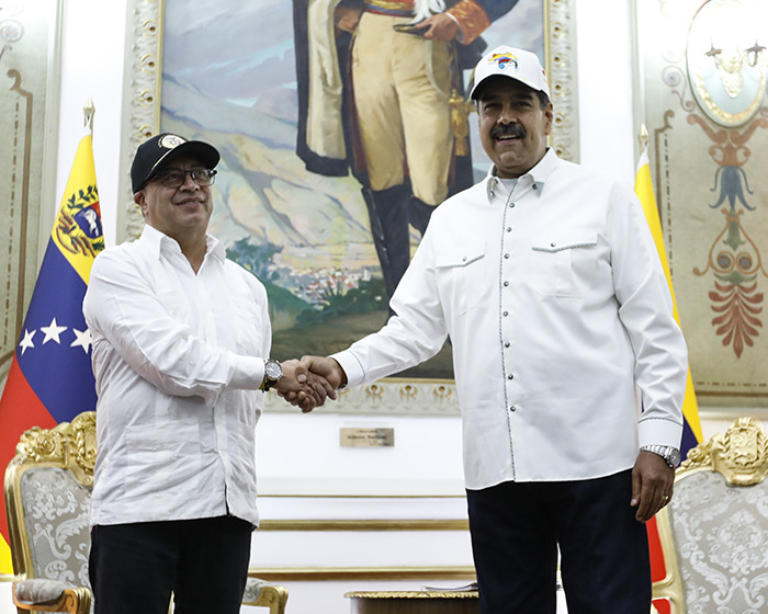 Venezuelan and Colombian presidents shaking hands in a formal setting with national flags and a large painting behind them.