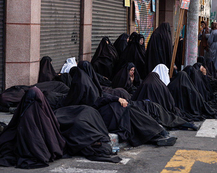 Group of women and children dressed in black, associated with Lev Tahor sect, gathered outside near closed shutters on highway.