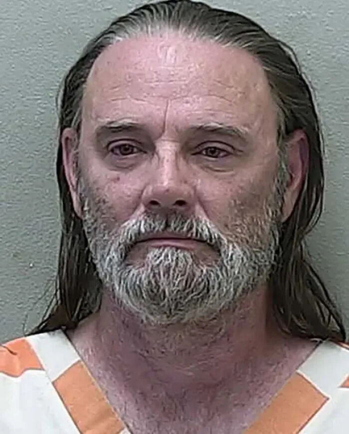 Middle-aged man with gray beard and long hair wearing an orange and white prison uniform, arrested over homicide case.
