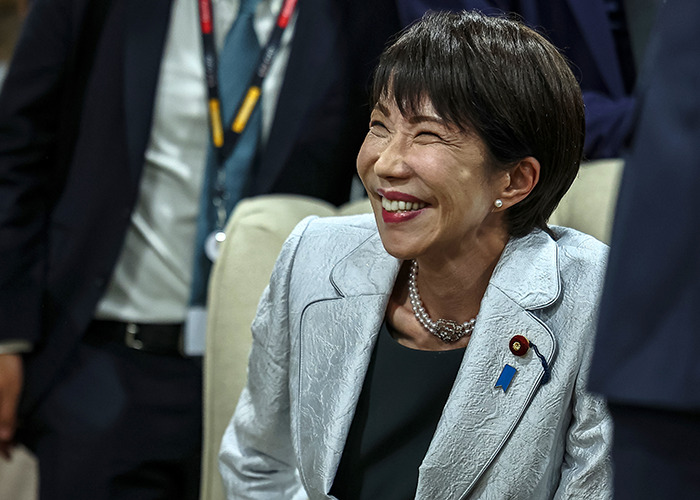 A smiling woman in a silver blazer at a G20 event focusing on new energy and global leadership discussions.