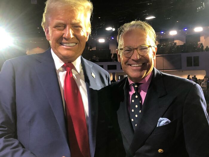 Donald Trump and another man smiling together at an indoor event with bright stage lighting, Mar-a-Lago setting.