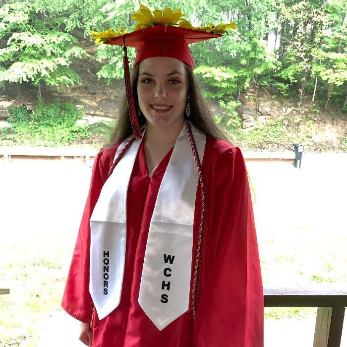Young woman in red graduation gown and cap with sunflowers, representing honor and achievement linked to National Guard member news.