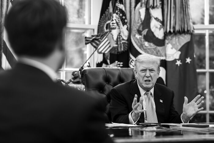 Former President Donald Trump speaking in the Oval Office with a man in the foreground, illustrating AI fact-checking claims.
