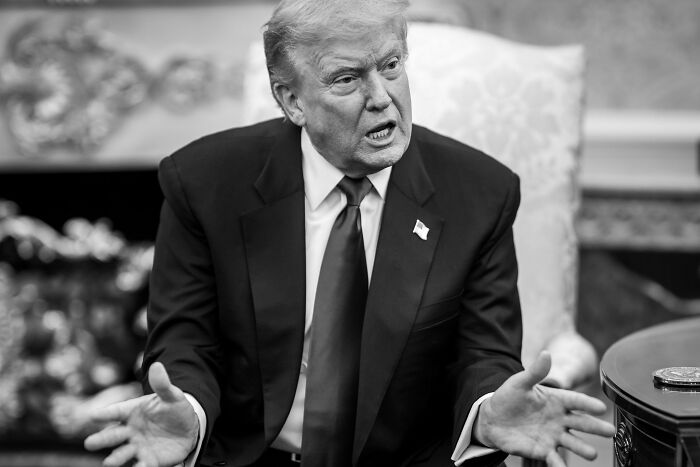Former President Donald Trump in a suit speaking passionately during a formal meeting in a decorated room.