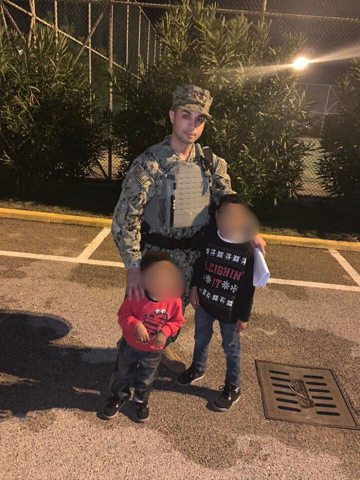 Navy sailor in uniform standing outdoors at night with two young children in casual clothes near a parking lot.