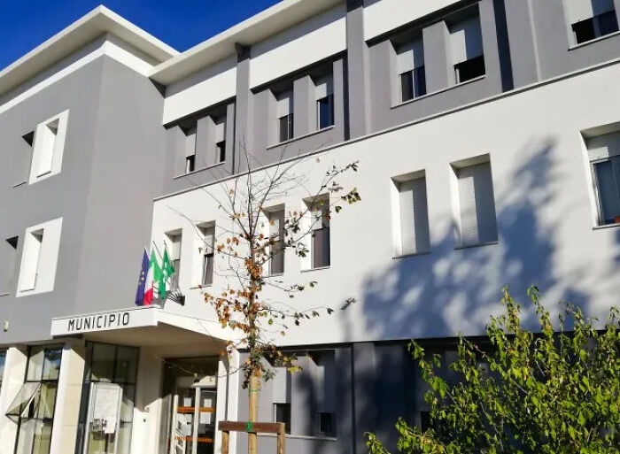 Municipal building exterior with flags and shadows, related to son accused of dressing as deceased mom pension plot.