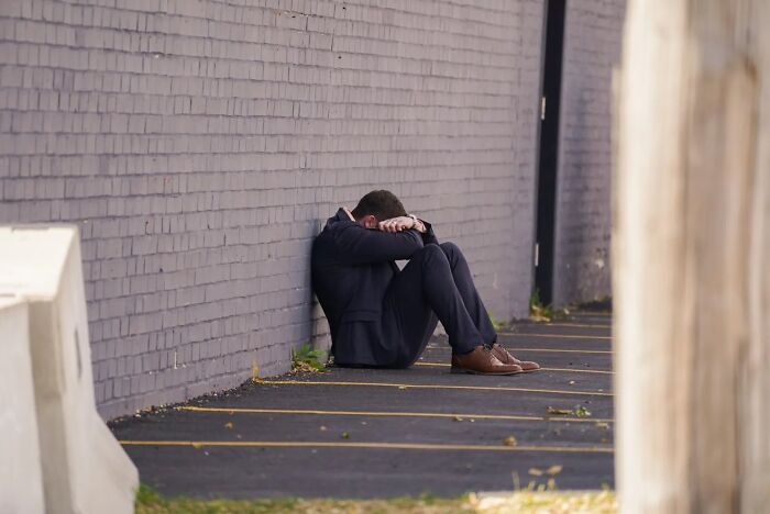 Man in tears sitting on ground by a wall, emotional after running to follow disappeared wife at ICE facility.