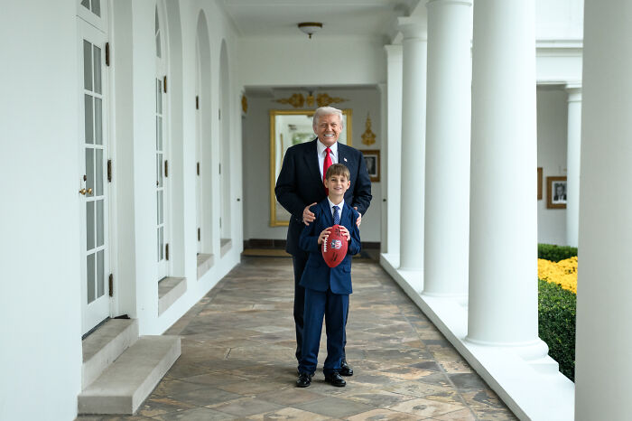 Donald Trump standing with his grandson holding a football in a corridor, raising health concerns about his walking.