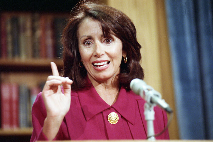 Nancy Pelosi speaking at a podium with a microphone, emphasizing a point during a historic congressional event.