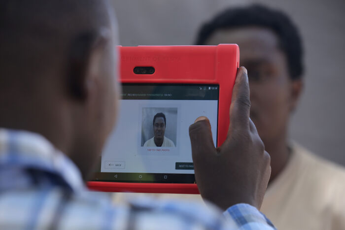 Person using a handheld device to capture biometric data as part of migration control surveillance systems.