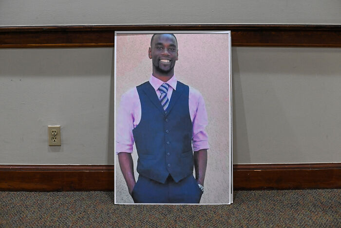 Framed portrait of a smiling man in a vest and tie resting against a wall related to traffic enforcement discussion.