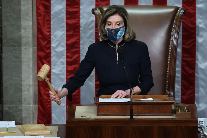 Nancy Pelosi holding a gavel in Congress chamber, wearing a mask during an official session at the podium.
