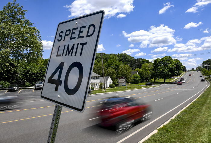 Speed limit sign on a suburban road with blurred red car illustrating challenges in traffic enforcement in America.