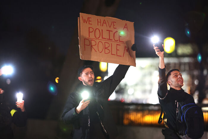 Protesters at night holding signs and lights, highlighting issues with police and traffic enforcement in America.