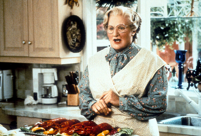 Man dressed as deceased mom in Mrs Doubtfire style plot to claim pension in a kitchen setting with seafood on table.