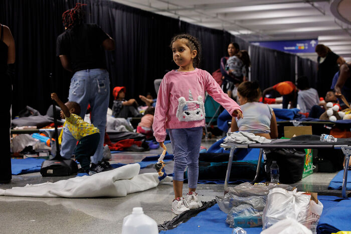Young girl standing in crowded airport area with migrants housed amid safety concerns under Biden administration policies