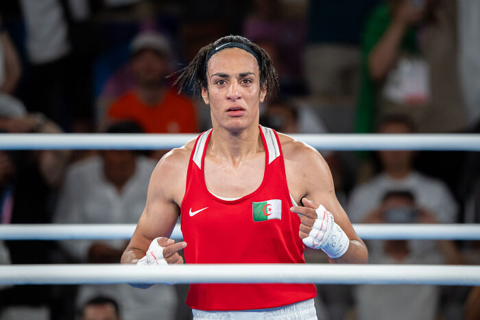 Boxer in red gear with Algerian flag inside a ring, illustrating Olympics poised to ban transgender and DSD competitors.