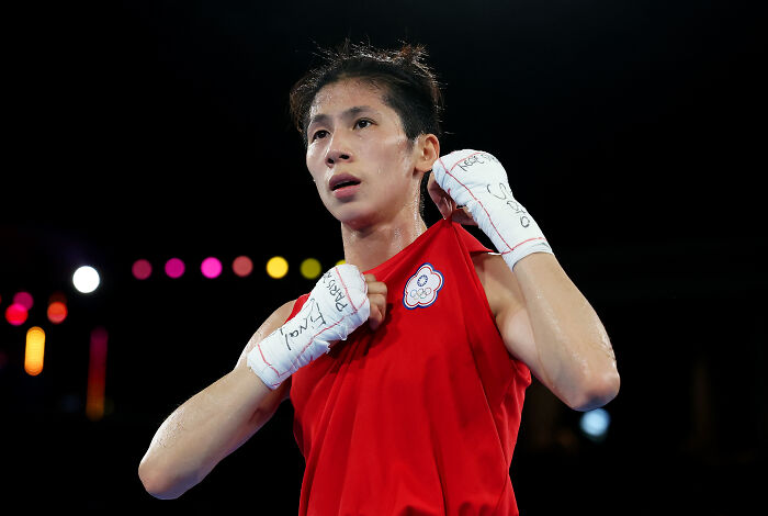 Olympic boxer adjusting red uniform in ring, highlighting debate on transgender and DSD competitors in sports competitions.