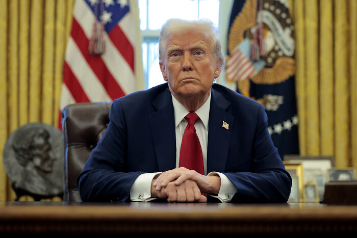Former president seated at a desk with American flags behind, symbolizing political conflict against Trump in NYC mayoral race.