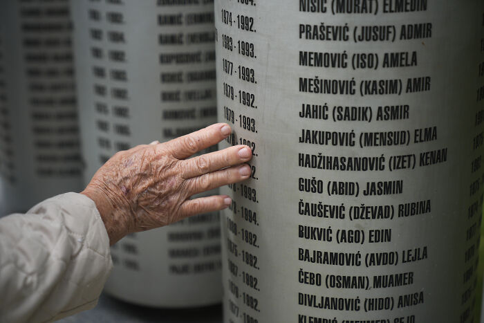 Hand of an elderly person touching a memorial wall with names, related to investigation of human safari tourists.