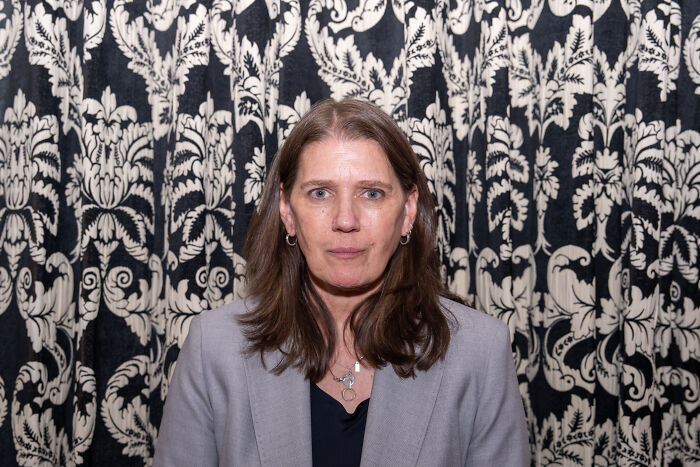 Woman with brown hair wearing a gray blazer against patterned background discussing Trump&rsquo;s niece dementia claims.