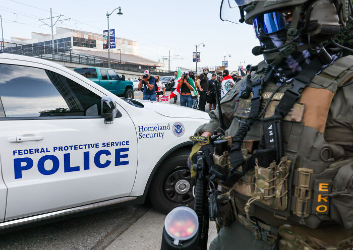 Heavily armed federal protective service police officer near Homeland Security vehicle during ICE raids protest.
