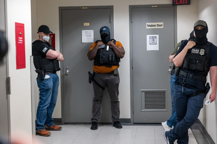 ICE officers in tactical gear standing in a hallway enforcing immigration policies involving a Native American woman case.