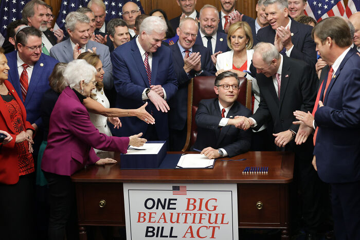 Group of politicians gathered around desk with One Big Beautiful Bill Act sign, illustrating ex-Trump fans losing hope in 2025.
