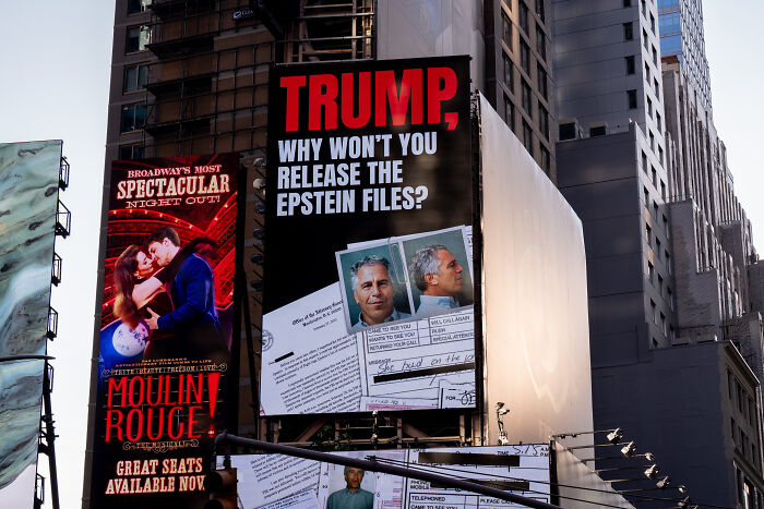 Billboard in a cityscape showing a message about Trump and the release of Epstein files with documents and photos.
