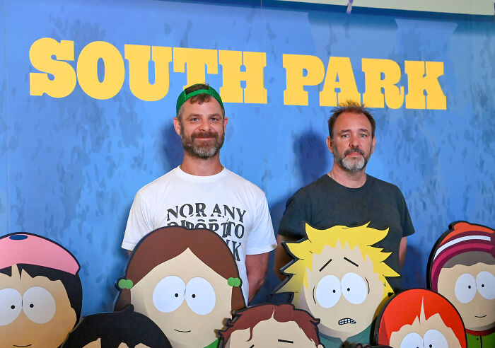 Creators of South Park posing behind cartoon character cutouts at a promotional event for the show featuring an intimate Trump-JD Vance scene.