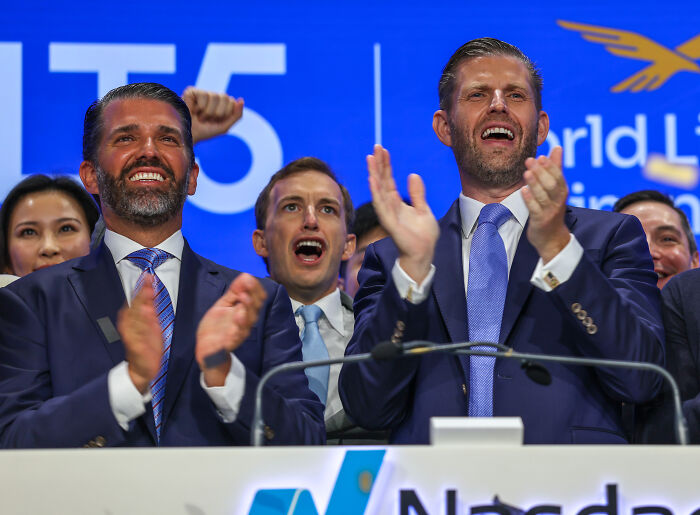 Two men in suits clapping enthusiastically at a podium during an event related to Trump pardoned crypto king linked to his sons.