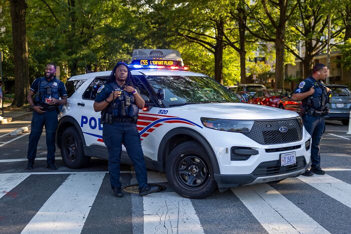 Three police officers standing by a marked patrol car during traffic enforcement on a city street.