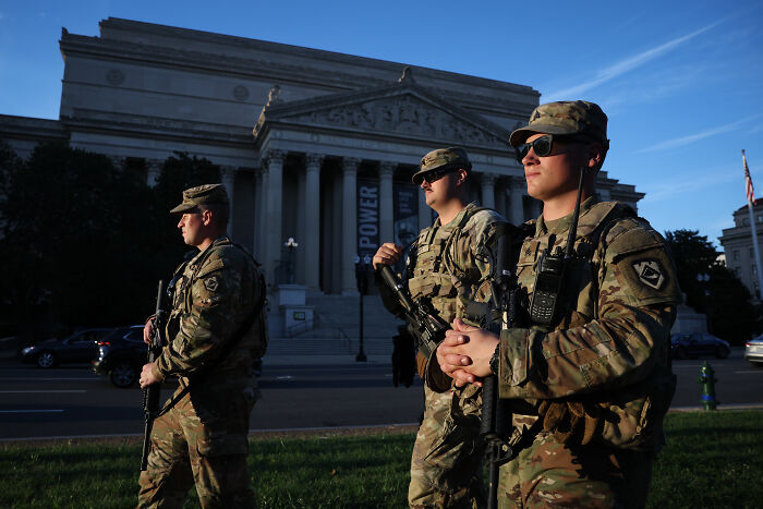 National Guard soldiers in uniform patrolling in front of a government building in Washington during daylight hours.